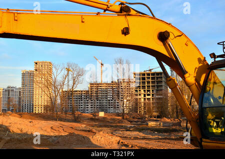 Baustelle mit mehrere Krane arbeiten an einem Gebäude Komplex, mit einem klaren blauen Himmel und Sonne. Blick durch Bagger Schaufel Stockfoto