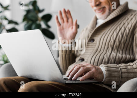 7/8-Ansicht der freundliche ältere Mann in Gläser Hand winken, während sie Videokonferenz Stockfoto