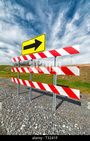 Vertikaler eine rot-weiß gestreifte Umweg Barriere mit einem Pfeil auf den Weg unter einem blauen bewölkten Himmel. Stockfoto