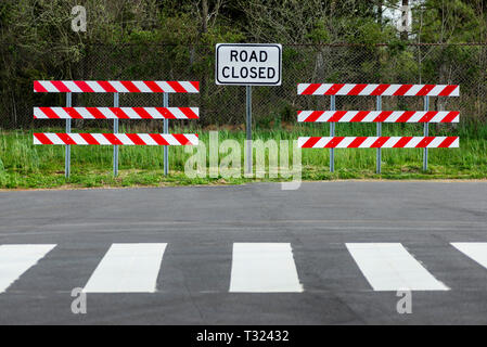 Horizontale Schuß von zwei rot-weiß gestreifte Schranken mit einer Straße geschlossen Zeichen in der Mitte von Ihnen. Es ist eine waldreiche Umgebung hinter Ihnen. Stockfoto