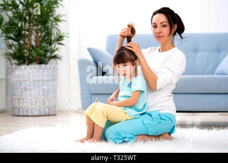 Glücklich liebende Familie. Mutter Kämmen ihrer Tochter sitzen auf dem Teppich auf dem Boden im Zimmer. Stockfoto