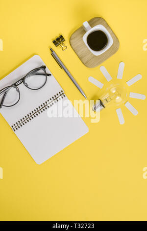 Ansicht von oben flach von Arbeitsbereich Schreibtisch gestalteten Design Büromaterial mit Stift, Notepad, Brillen, Tasse Kaffee und Glühbirne auf eine gelbe Farbe Papier bac Stockfoto