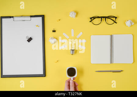 Flach brainstorming Tabelle Ansicht von oben. Leere Clip Board, Bürobedarf, Kugelschreiber, Notizblock, Brillen, Tasse Kaffee in der Hand, Glühbirne auf Gelb backgr Stockfoto