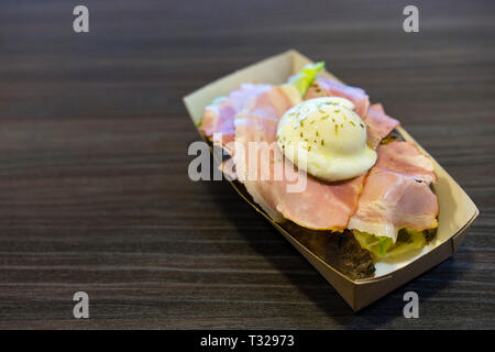 Imbiss mit gebackenen Kartoffeln, Speck und pochierte Eier in einem Karton auf einem Schwarzen Tisch. Stockfoto