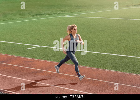 Junge Frau Athlet auf Stadion sportlicher Lifestyle läuft auf der Schiene das Einatmen von konzentrierten Stockfoto