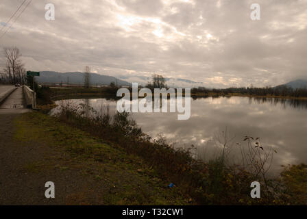 Am ruhigen Ufer des Vedder River spiegelt sich ein turbulenter grauer, bedeckter Himmel in Chilliwack, British Columbia, Kanada, wider Stockfoto