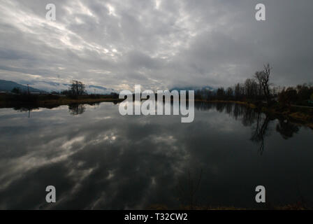 Am ruhigen Ufer des Vedder River spiegelt sich ein turbulenter grauer, bedeckter Himmel in Chilliwack, British Columbia, Kanada, wider Stockfoto