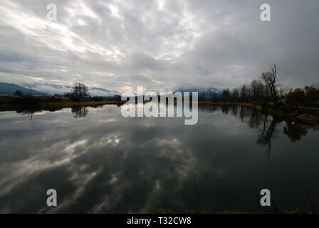 Am ruhigen Ufer des Vedder River spiegelt sich ein turbulenter grauer, bedeckter Himmel in Chilliwack, British Columbia, Kanada, wider Stockfoto