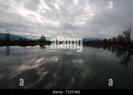 Am ruhigen Ufer des Vedder River spiegelt sich ein turbulenter grauer, bedeckter Himmel in Chilliwack, British Columbia, Kanada, wider Stockfoto