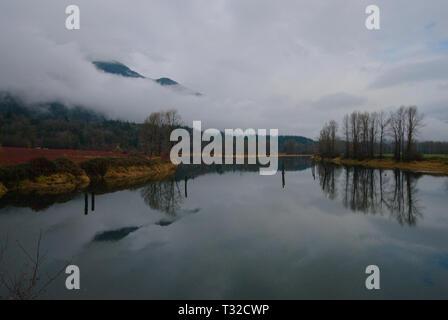 Am ruhigen Ufer des Vedder River spiegelt sich ein turbulenter grauer, bedeckter Himmel in Chilliwack, British Columbia, Kanada, wider Stockfoto