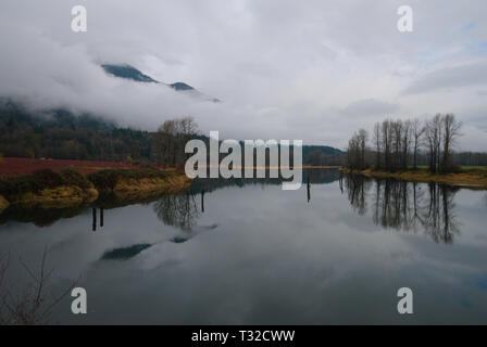 Am ruhigen Ufer des Vedder River spiegelt sich ein turbulenter grauer, bedeckter Himmel in Chilliwack, British Columbia, Kanada, wider Stockfoto