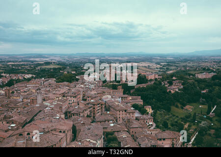 Panoramablick auf Siena Stadt mit historischen Gebäuden und weit weg die grünen Felder von Torre del Mangia ist ein Turm in der Stadt. Sommer sonnigen Tag und dramatische Stockfoto