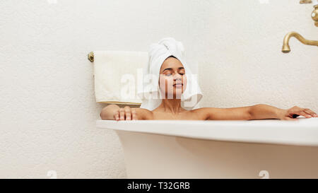 Frau mit weißen Handtuch auf dem Kopf entspannen in der Badewanne mit geschlossenen Augen Stockfoto