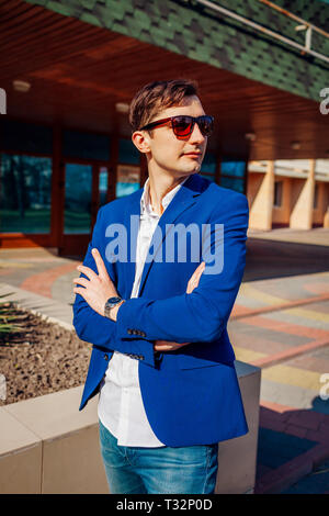 Glückliche junge stilvollen Mann posiert im Freien mit Hände gekreuzt. Hübscher Kerl trägt klassische Kleidung und Accessoires. Die Spring Street Fashion. Stockfoto