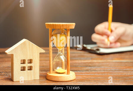 Holz- Haus und die Uhr. Eine Person, die Dokumente signiert. Die Unterzeichnung eines Vertrags ein Haus oder eine Wohnung zu mieten. Ein. Testament. Kauf oder Sellin. Stockfoto