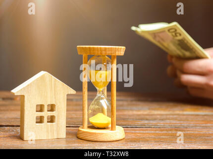 Holz- Haus und die Uhr. Unternehmer zählen Geld. Die Zahlung der Anzahlung oder Vorauszahlung für die Miete ein Haus oder eine Wohnung. Langfristige Hypothek auf die h Stockfoto