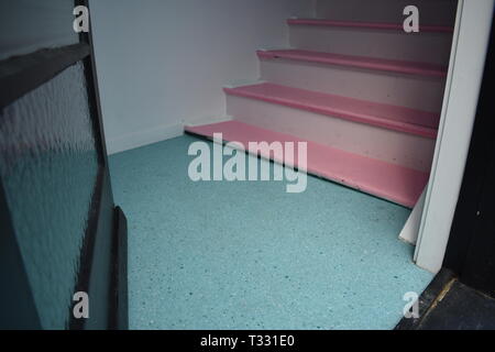 Eine Glastür führt auf einen lino Stock und rosa bemalten hölzernen Treppen in einem älteren Gebäude Stockfoto