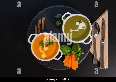 Leckeren, gesunden Brokkoli und Butternut oder Kürbis Suppen aus frischem Gemüse garniert mit Sahne gesehen von oben nach unten in einer kreisförmigen Holz schwarz b Stockfoto