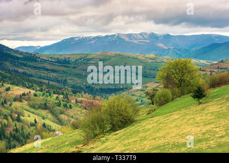 Ländliche Landschaft in den Bergen. Dorf, die in der fernen Berge. landwirtschaftliche Felder auf Hügeln. Bäume auf grasigen Hang. wunderbaren Frühling Landschaft o Stockfoto