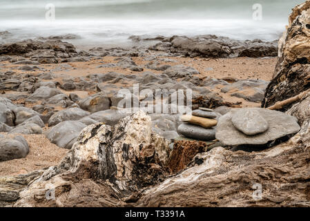 Ein Stein Haufen auf einen Baumstamm auf einem steinigen Strand, an Cocklawburn Beach in der Nähe von Berwick-upon-Tweed in Northumberland, England, Großbritannien Stockfoto