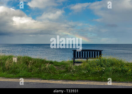 Eine Bank mit einem Regenbogen über der Nordsee Küste, im Benthall, Northumberland, England, UK gesehen Stockfoto