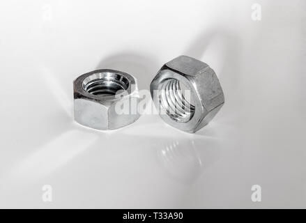 Paar silberfarbenen Metall glänzend große Schrauben Muttern auf Weiß mit Reflexionen und Schatten Stockfoto