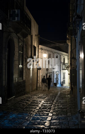 Lampen leuchten auf Stein Kopfsteinpflaster in der Nacht als touristische Paar Spaziergang entlang der gepflasterten Straße Gasse in Erice, Sizilien, Italien Stockfoto