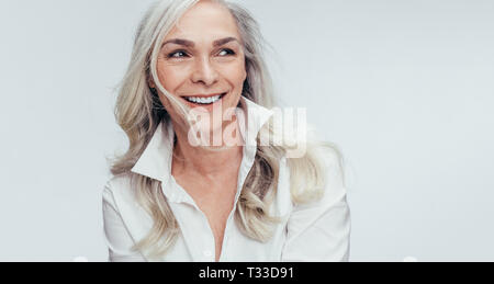 Elegante Mitte der erwachsenen Frau gegen den weißen Hintergrund. Stilvolle reife Frau in Weiß casuals weg schauen und lächeln. Stockfoto