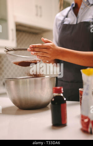 In der Nähe der weiblichen Konditor sichten Schokolade Mehl in eine Schüssel Teig in der Küche zu machen. Frau sieben das Mehl während der Kuchen vorbereiten. Stockfoto