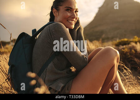 Junge Frau Rest nehmen beim Wandern in der Natur. Weibliche Wanderer sitzen auf einer Rasenfläche und lächelnd. Stockfoto