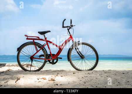 Red Vintage Fahrrad auf weißen Sandstrand über blaue Meer und dem klaren, blauen Himmel Hintergrund, Frühling oder Sommer Urlaub Konzept. Fahrrad geparkt durch die Stockfoto