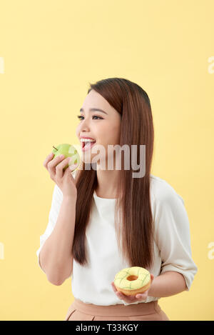 Die richtige Wahl für gute Gesundheit aus. Frauen ist die Wahl Wahl zwischen Donut und Apfel grün über gelb isoliert. Stockfoto