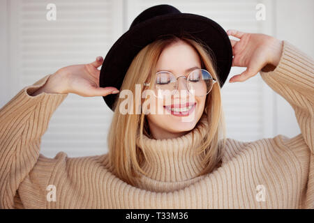 Charmante junge Mädchen in einem stylischen Hut und Brille. Junge Frau Zahnspange tragen und lächelnd. Close-up Portrait auf einen hellen Hintergrund Stockfoto