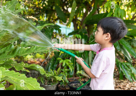 Kinder sind Bewässerung von Pflanzen mit Gummischlauch in den Garten. Stockfoto