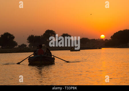 Die Leute, die eine Bootsfahrt auf Gadi Sagar See in Jaisalmer bei Sonnenuntergang mit der Sonne im Hintergrund Stockfoto