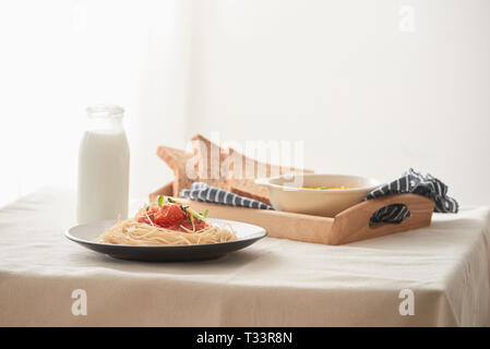 Hausgemachte Spaghetti mit Tomatensauce in einem weißen Teller auf dem Tisch mit kürbispüree, Milch und Toast. Stockfoto