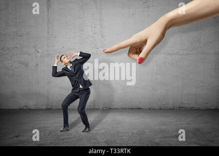 Kleine Unternehmer lehnen nach links und über seinen Kopf mit den Händen versuchte, sich aus der Hand des großen Frau auf der rechten Seite zu schützen. Stockfoto