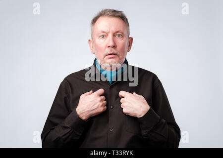 Kaukasische reifer Mann im schwarzen T-Shirt auf sich selbst zeigt mit Frage, ob er etwas falsch gemacht haben. Stockfoto