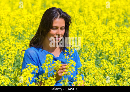 Junge kolumbianische Frau auf der Suche nach Blume gelb blühende Raps Feld Stockfoto