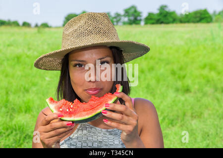 Junge kolumbianische Frau Stroh Sommer Hut essen frische rote Melone in niederländischen Natur Stockfoto