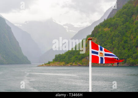 Norwegen Fahne winken auf dem Hintergrund der Fjord in Norwegen. Winkende norwegische Flagge auf dem Fjord von Bergen Hintergrund umgeben. Trübe Sommerwetter in Norwegisch Stockfoto