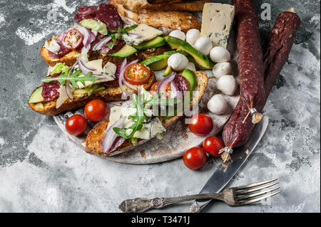 Köstliche Sandwiches mit geräucherter Wurst, Avocado, Käse, Tomaten, roten Zwiebeln und Rucola. Stockfoto