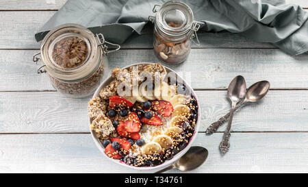 Gesundes Frühstück Schüssel: Quark, Müsli, Bananen, Erdbeeren, Heidelbeeren und Puffreis. Holztisch Hintergrund. Ansicht von oben Stockfoto