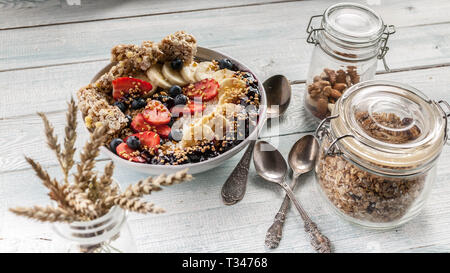 Bio-frühstück. Gesundes Frühstück Schüssel: Quark, Müsli, Bananen, Erdbeeren, Heidelbeeren und Puffreis. Holztisch Hintergrund Stockfoto