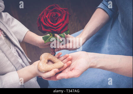 Das Mädchen gibt ihre Mutter eine Rose und herzförmige Plätzchen. Mutter und Tochter die Hände. Muttertag Konzept Stockfoto