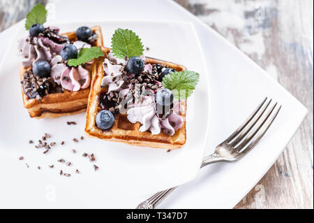 Belgische Waffeln mit Sahne, Marmelade, Blaubeeren und Minze auf einer weißen Platte. Close-up. Köstliches Dessert Stockfoto