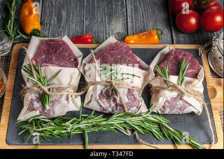 Rohes Fleisch Steaks und Rosmarin. Frisches Fleisch auf einem Schneidebrett, Kräuter und Gemüse Stockfoto