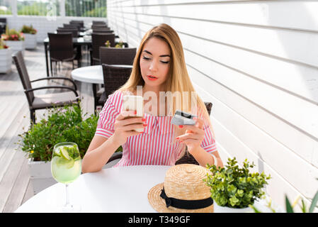 Eine Frau in einem Café im Sommer in der Stadt, zahlt Mittagessen Frühstück Abendessen, Kunststoff Kreditkarte, online im Internet. Meldet sich mit einem Passwort, Lastschriften Geld Stockfoto