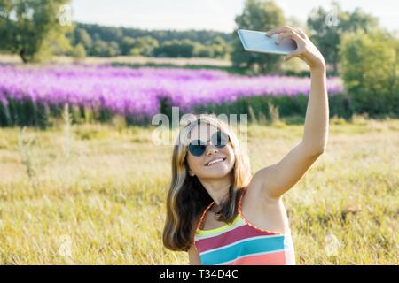 Junge Mädchen teenager Wandern in der Natur ist auf Mobile Smartphone fotografiert, sonnigen Sommertag Hintergrund lila Lavendel Feld. Stockfoto