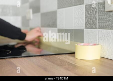 Worker protecting countertop in kitchen with masking tape before starting construction repairs with ceramic tiles. Stockfoto